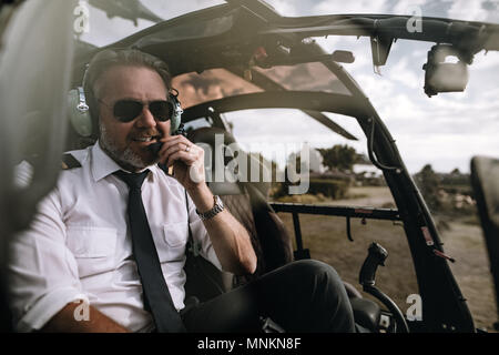 Happy helicopter pilot with headset in the helicopter. Male pilot talking on the headset in the cockpit of a helicopter. Stock Photo