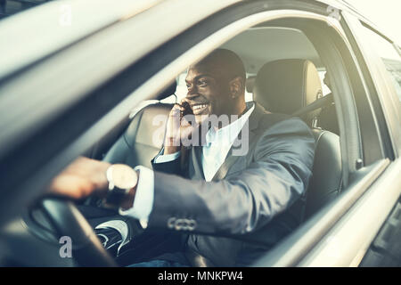 Smiling African businessman talking on a cellphone while sitting in his car before his morning commute to work Stock Photo