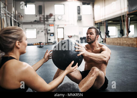Two fit young people in sportswear exercising together with a medicine ball on the floor of a gym during a workout session Stock Photo