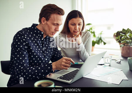 Two business colleagues talking and working online with a laptop while sitting together at a desk in an office Stock Photo