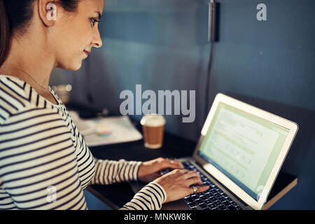 Focused young designer sitting at a table in a modern office working online with a laptop Stock Photo