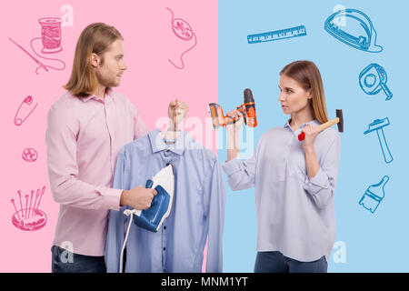 Man with an iron feeling surprised while seeing his wife holding instruments Stock Photo