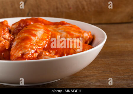 Marinated chicken wings in a white bowl over wooden background - close-up view Stock Photo