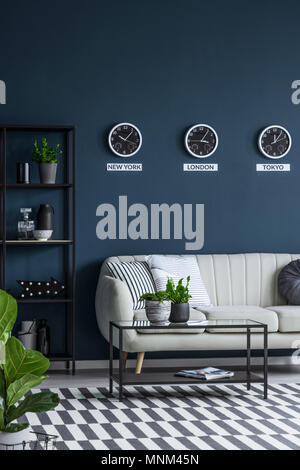 Green plants in a classy, navy blue living room interior with beige couch and checkered rug Stock Photo