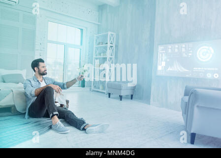 Cheerful designer looking happy while using a remote control at home Stock Photo