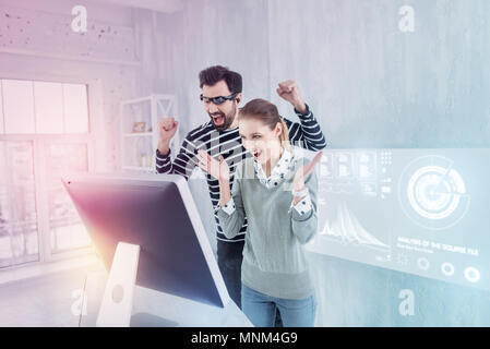 Happy colleagues putting their hands up and shouting Stock Photo