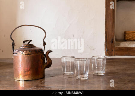 Still life with a beautiful worn retro style copper tea kettle with three empty glasses on a massive wooden table. Stock Photo