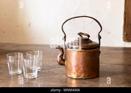 Still life with a beautiful worn retro style copper tea kettle with three empty glasses on a massive wooden table. Stock Photo