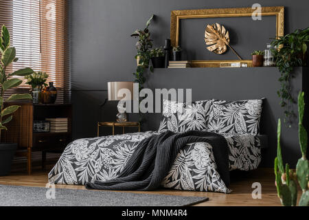 An old-fashioned wooden cabinet and an elegant golden leaf in frame art in a dark gray luxurious bedroom interior Stock Photo