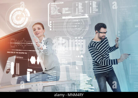 Young designer sitting on the table and her colleague working near Stock Photo