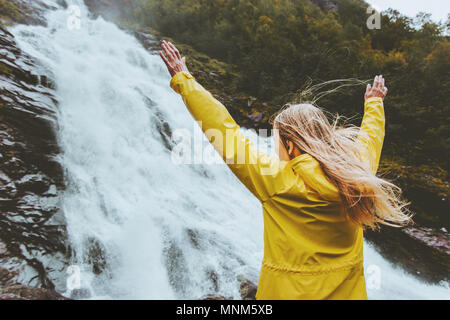 Traveler woman raised hands enjoying waterfall landscape Traveling alone into the wild adventure lifestyle harmony with nature concept emotional expre Stock Photo