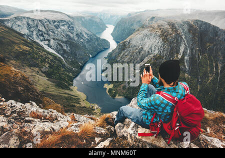 Man traveler using smartphone sitting on mountain summit travel in Norway adventure lifestyle active vacations modern technology connection concept Stock Photo