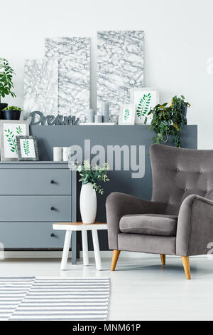 Paintings, grey chest of drawers and comfortable armchair in a modern living room interior Stock Photo
