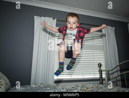 A little boy jumps on a bed in a bedroom / Child jumping on bed Stock Photo