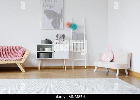 Decorative pink rabbit cushion lying on bright small sofa in baby room Stock Photo
