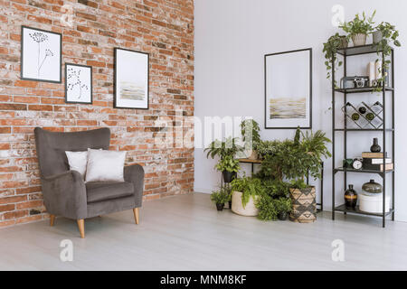 Poster on white wall above plants in simple living room with grey armchair against brick wall Stock Photo