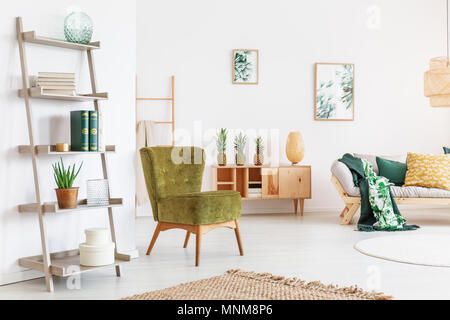 Pear green chair and yellow pillow on beige sofa in cozy room with accessories on wooden shelf Stock Photo