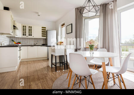 Light stylish interior with round table, white chairs and functional open kitchen