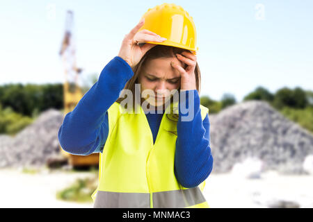 Young female engineer or architect suffering headache because of stressful job as exhausted employee concept on construction site background Stock Photo
