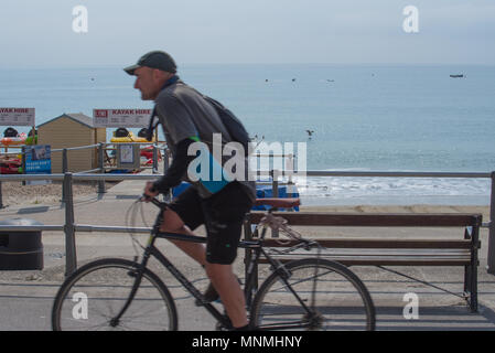 Lyme Regis, Dorset, UK. 18th May 2018. UK Weather: A cyclist rides along the seafront on a bright and sunny morning in Lyme Regis. Credit: PQ/Alamy Live News Stock Photo