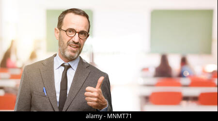 Teacher man using glasses smiling broadly showing thumbs up gesture to camera, expression of like and approval at classroom Stock Photo
