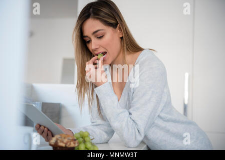 Young woman eating white grapes and using digital tablet Stock Photo