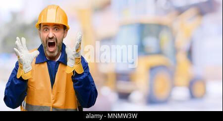 Senior engineer man, construction worker stressful keeping hands on head, terrified in panic, shouting at work Stock Photo