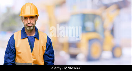 Senior engineer man, construction worker with sleepy expression, being overworked and tired at work Stock Photo