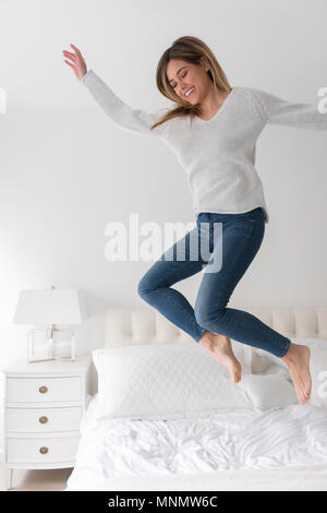 Young woman jumping in bedroom Stock Photo