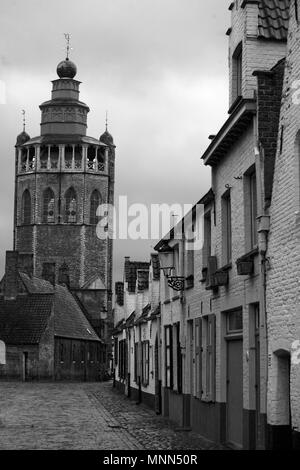 Balstraat, Brugge, Belgium: the Jeruzalemkerk, with traditional whitewashed cottages on the quiet cobbled street in the foreground; black and white Stock Photo