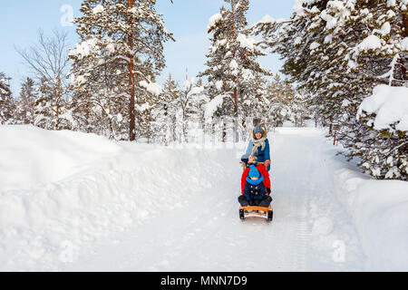 Beautiful family of mother and kids enjoying snowy winter day outdoors having fun sledging Stock Photo