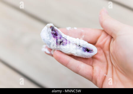 Female, woman hand holding piece of mochi sticky glutinous rice cake dessert filled with purple blueberry tahini sesame seed paste peanut butter jam f Stock Photo