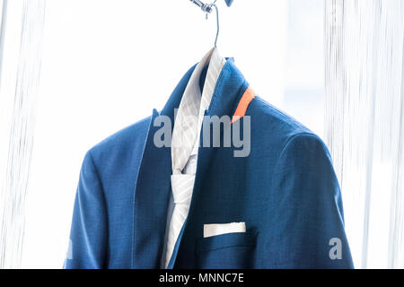 Men's new marine navy blue suit and tie groom closeup wedding preparation isolated, pocket handkerchief hanging on window hanger in bright room isolat Stock Photo