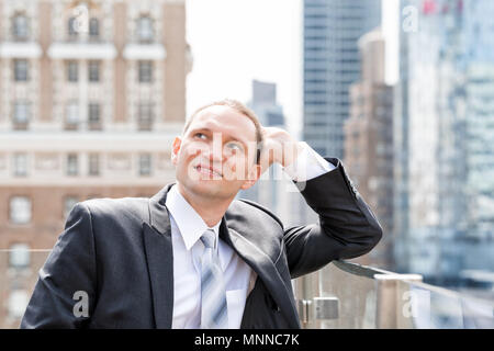 Handsome, attractive young happy smiling businessman closeup face portrait standing in suit, tie, looking up on New York City cityscape skyline in Man Stock Photo