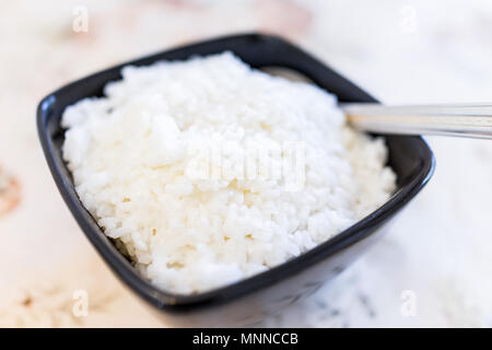 Macro closeup of plain white boiled short or medium grain rice in black bowl, serving spoon on table showing detail and texture Stock Photo