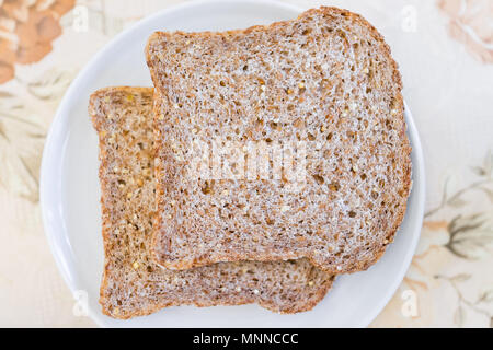 Closeup of two slices pieces of whole wheat sprouted toasted grain bread on plate, plain simple on table macro flat top down view Stock Photo