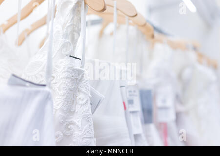 Many wedding dresses with price tags in boutique discount store, white garments hanging on rack hangers row closeup with white lace, tulle, design Stock Photo