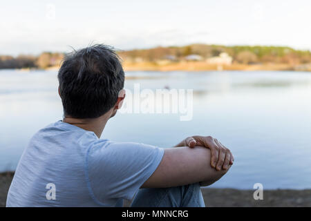 Lake Fairfax Park in winter in Reston, Virginia with young sad man sitting at blue lake at sunset looking in Northern VA closeup Stock Photo