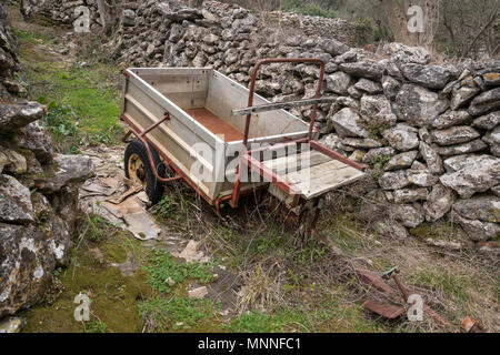 Small old rusty trailer standing near a stone wall (Island Cres, Croatia) Stock Photo