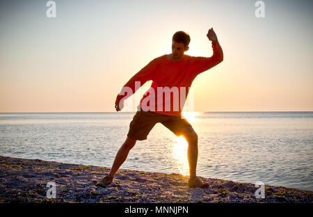 Young attractive man making Thai-chi movements on the beach of Black sea Stock Photo
