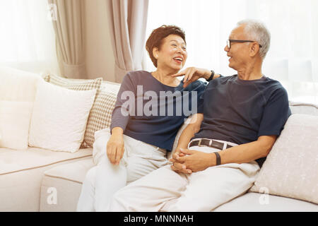 Romantic senior Asian couple laughing and sitting on sofa at home Stock Photo