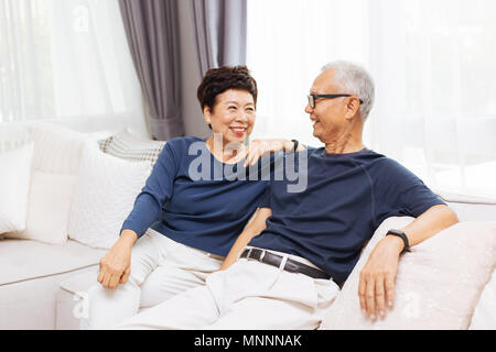 Romantic senior Asian couple laughing and sitting on sofa at home Stock Photo