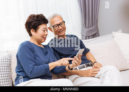 Senior Asian couple grandparents using a smart phone together on sofa at home Stock Photo