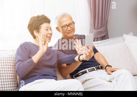 Senior Asian couple grand parents making a video call and waving at the caller Stock Photo