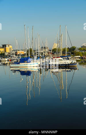 Close up view of sailing boats berthed in the marina in Cardiff Bay in early morning light with reflections in perfectly still water Stock Photo