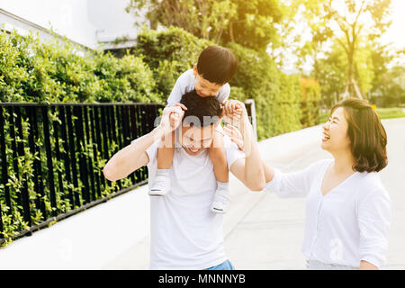 Cute Asian father piggybacking his son along with his wife in the park. Excited family spending time together with happiness