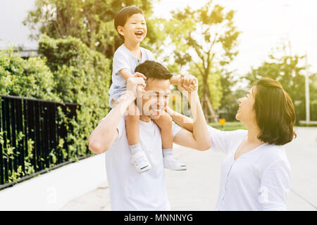 Cute Asian father piggybacking his son along with his wife in the park. Excited family spending time together with happiness