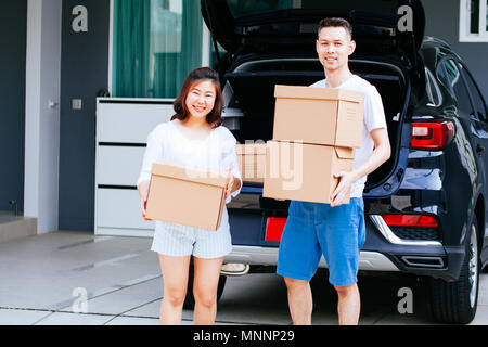 Mature happy Asian married couple carrying cardboard boxes from car trunk at new home Stock Photo