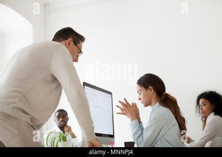 Angry boss scolding or firing upset intern in multiracial office Stock Photo