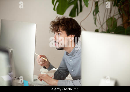 Funny surprised employee eating chinese food looking at computer Stock Photo